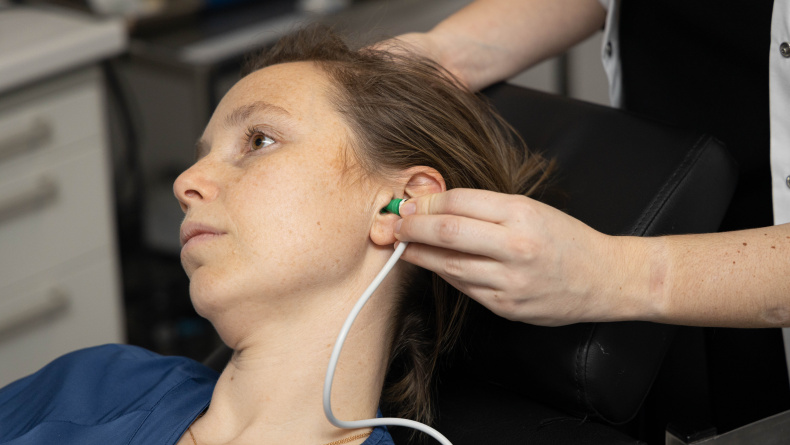 Een vrouw tijdens een OAE onderzoek met dopjes in de oren