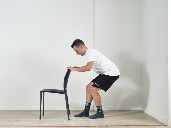Hou handen op leuning van stoel en doe squat