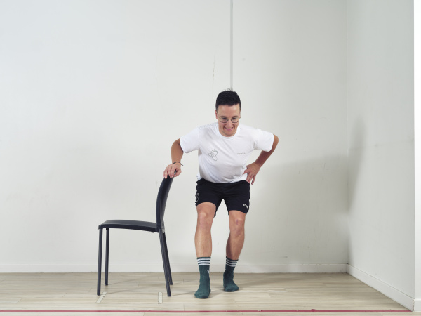 Hand op leuning stoel en doe een squat